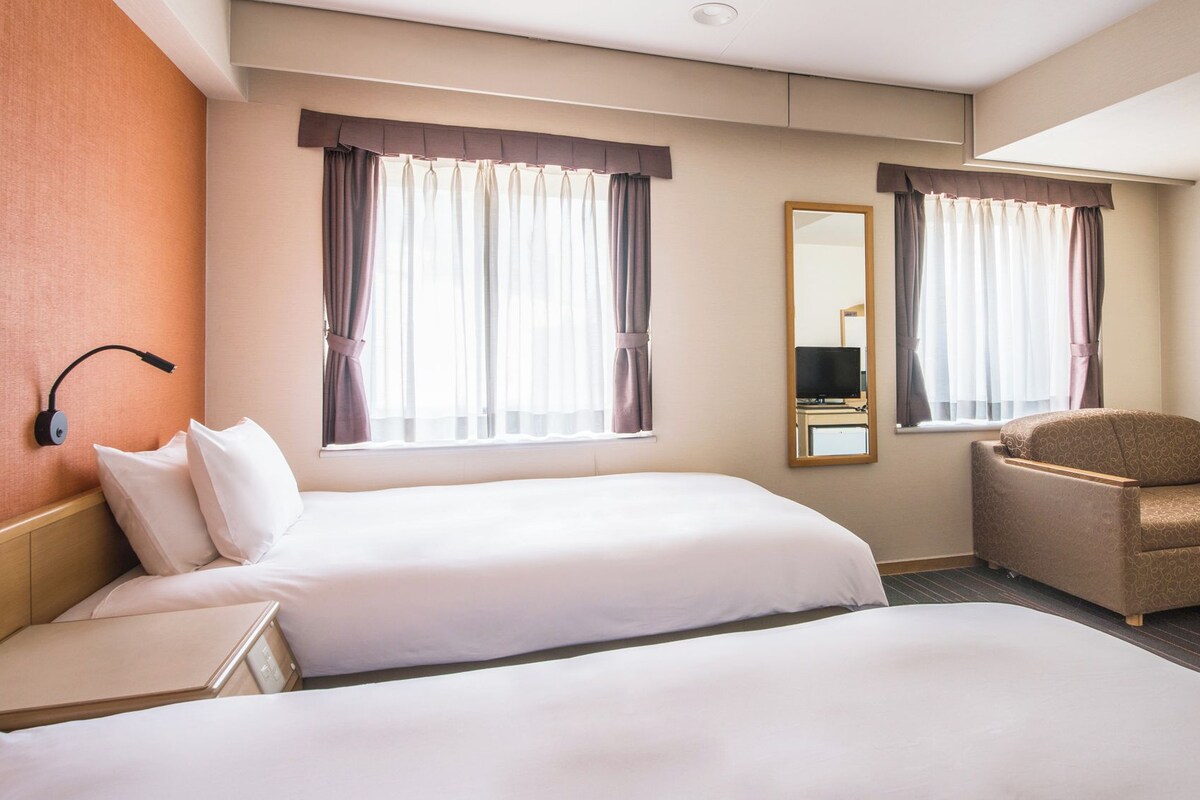 A hotel room with two beds, a chair, a desk, and a mirror.