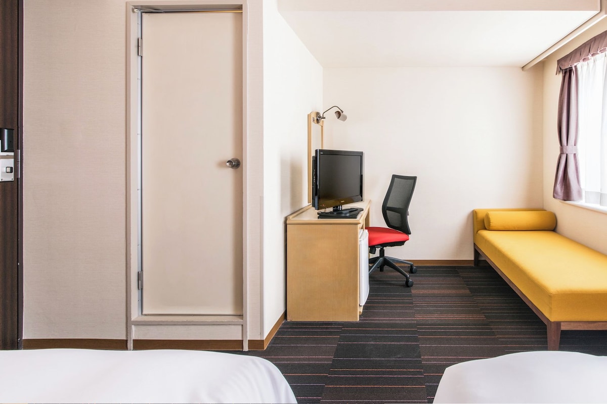 A hotel room with two beds, a desk with a computer, a chair, and a sofa.
