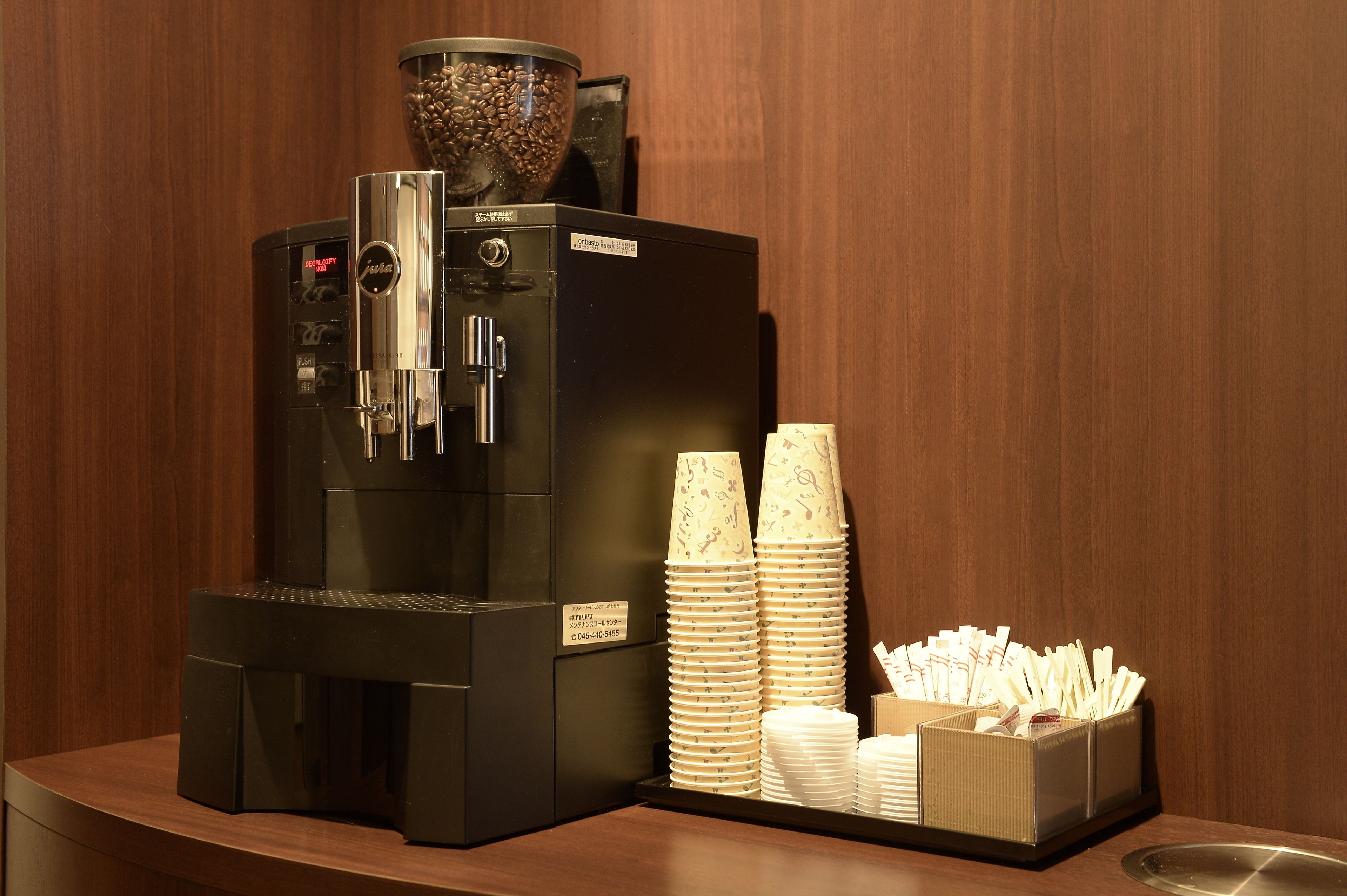 Una máquina de café con un depósito para granos, vasos desechables apilados y un dispensador de servilletas sobre una encimera.