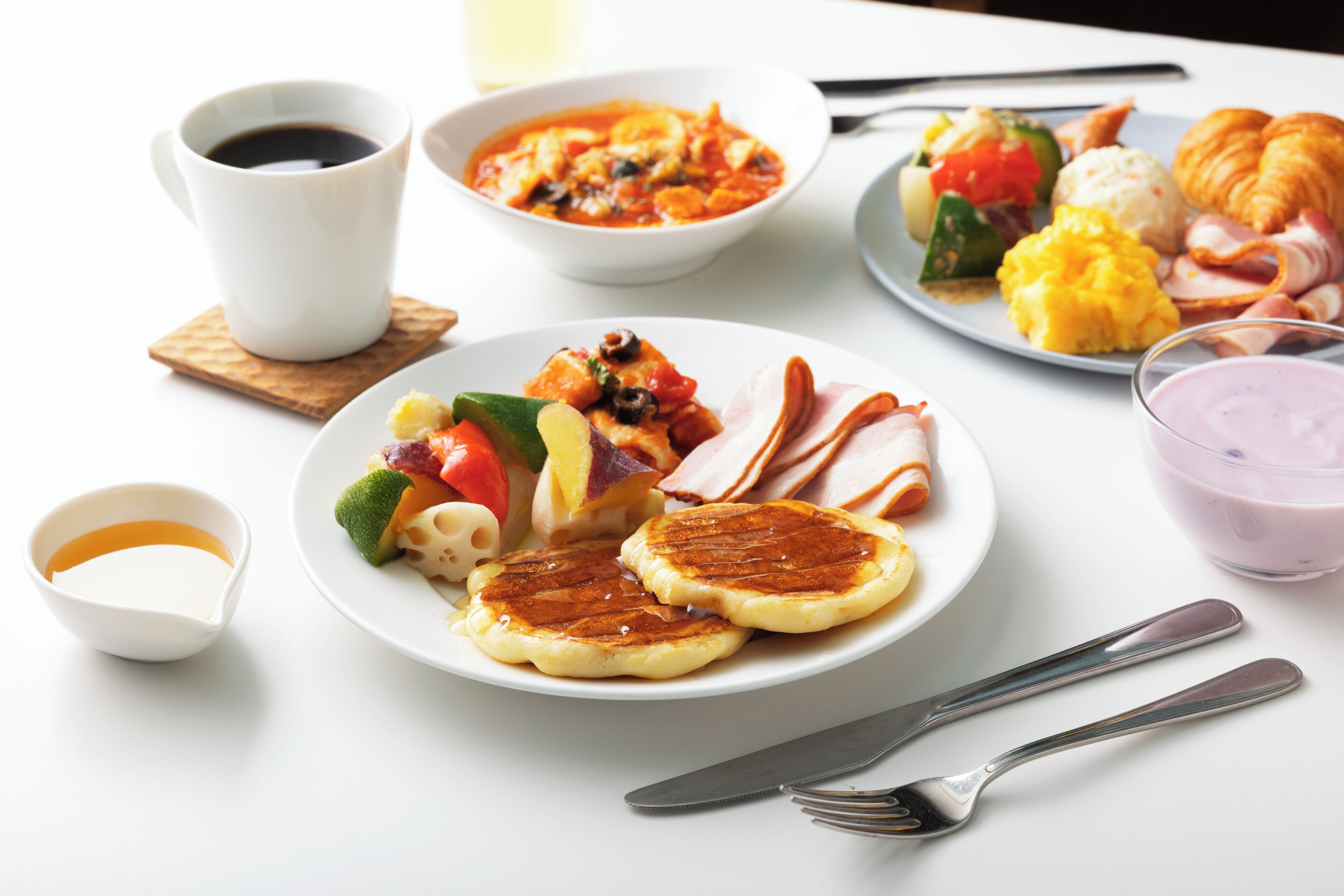 A breakfast table with pancakes, eggs, bacon, and a cup of coffee.
