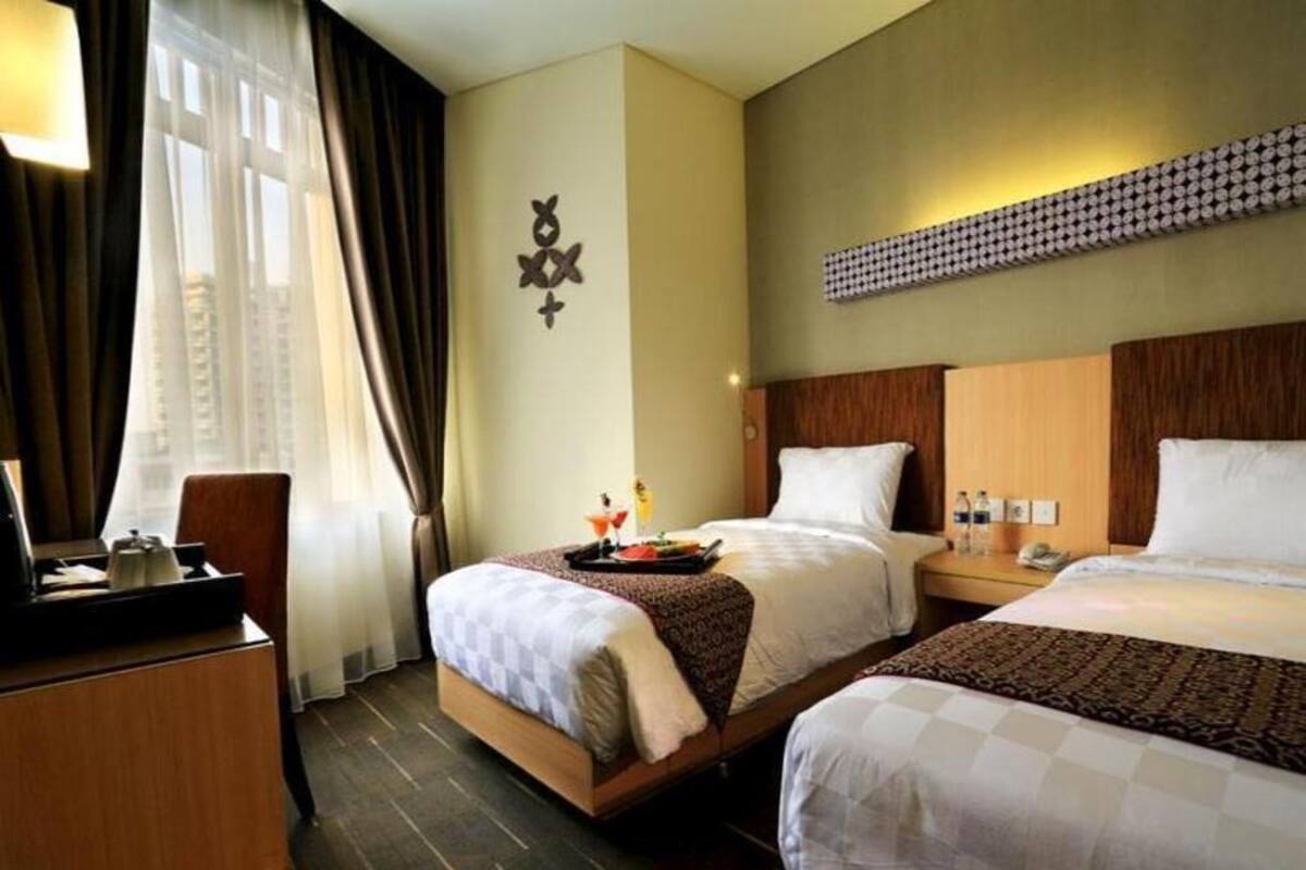 Habitación de hotel con dos camas, un escritorio, una lámpara, una ventana con cortinas y un adorno en la pared.