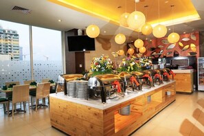 A buffet setup with multiple food dispensers, a wooden counter, and a seating area with chairs and tables. - Cipta Hotel Pancoran (Jakarta)