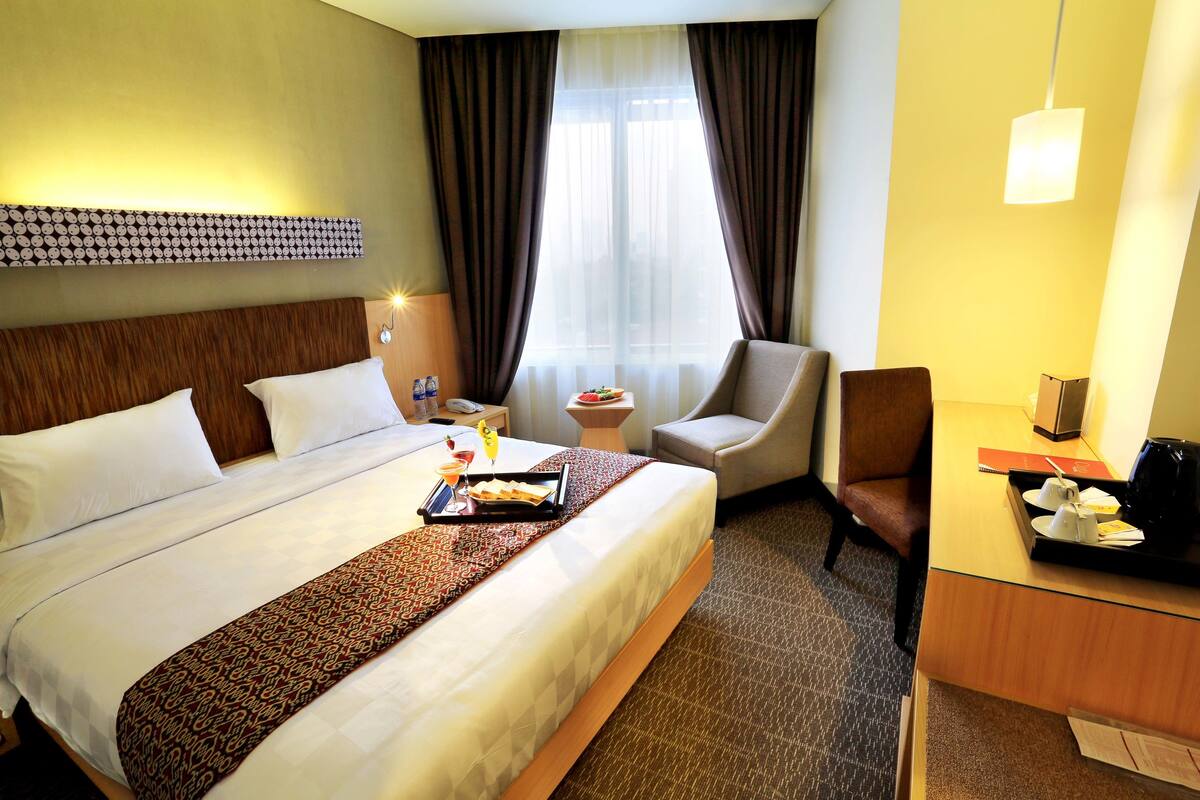 Una habitación de hotel con una cama grande, un escritorio, una silla y una pequeña mesa con una bandeja de desayuno.