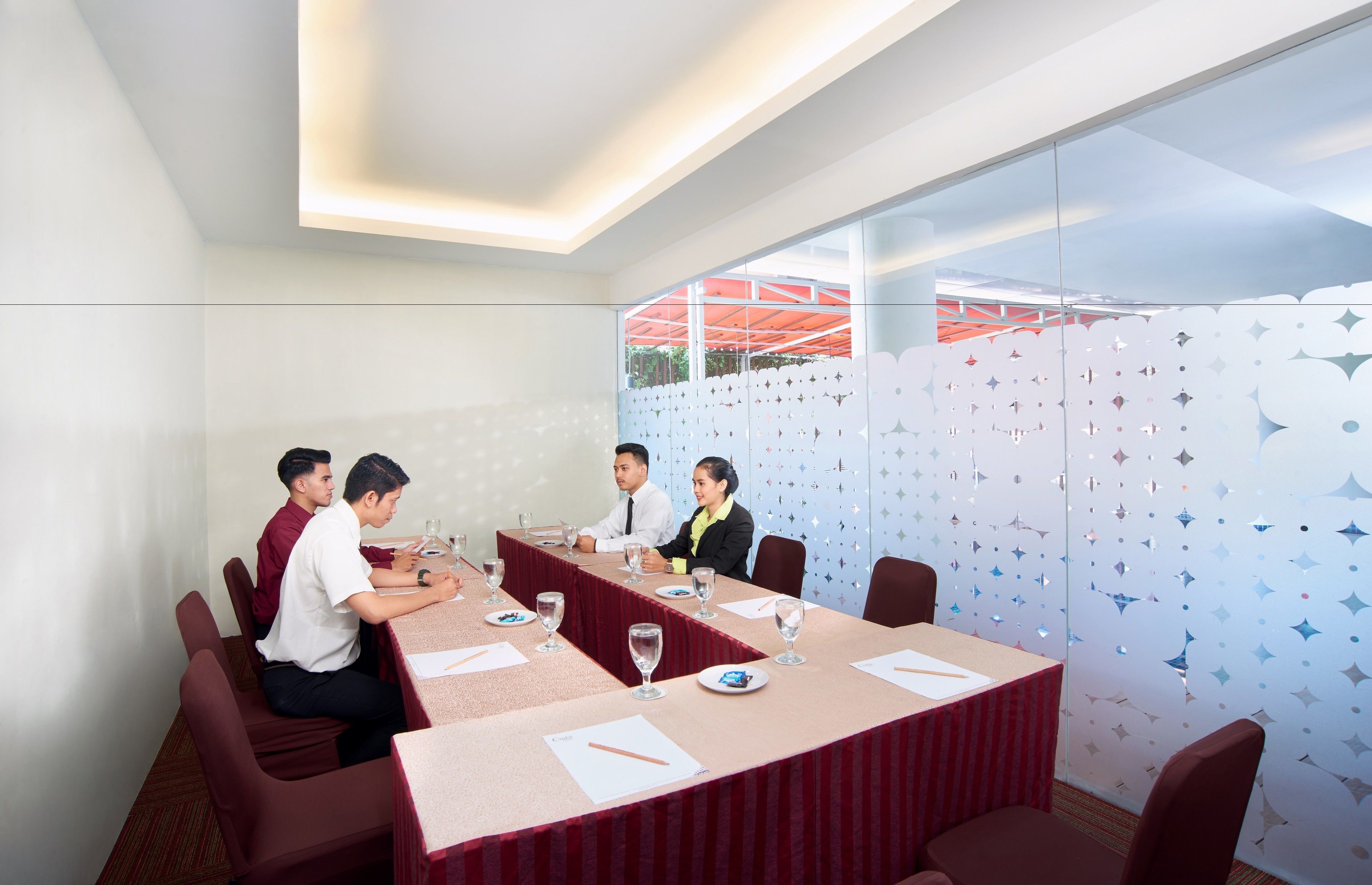 A conference room with a long table, chairs, and a glass partition with a geometric pattern.