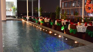 A poolside dining area with tables set for a meal, surrounded by chairs with green sashes, and a decorative arch with lights. - Cipta Hotel Pancoran (Jakarta)