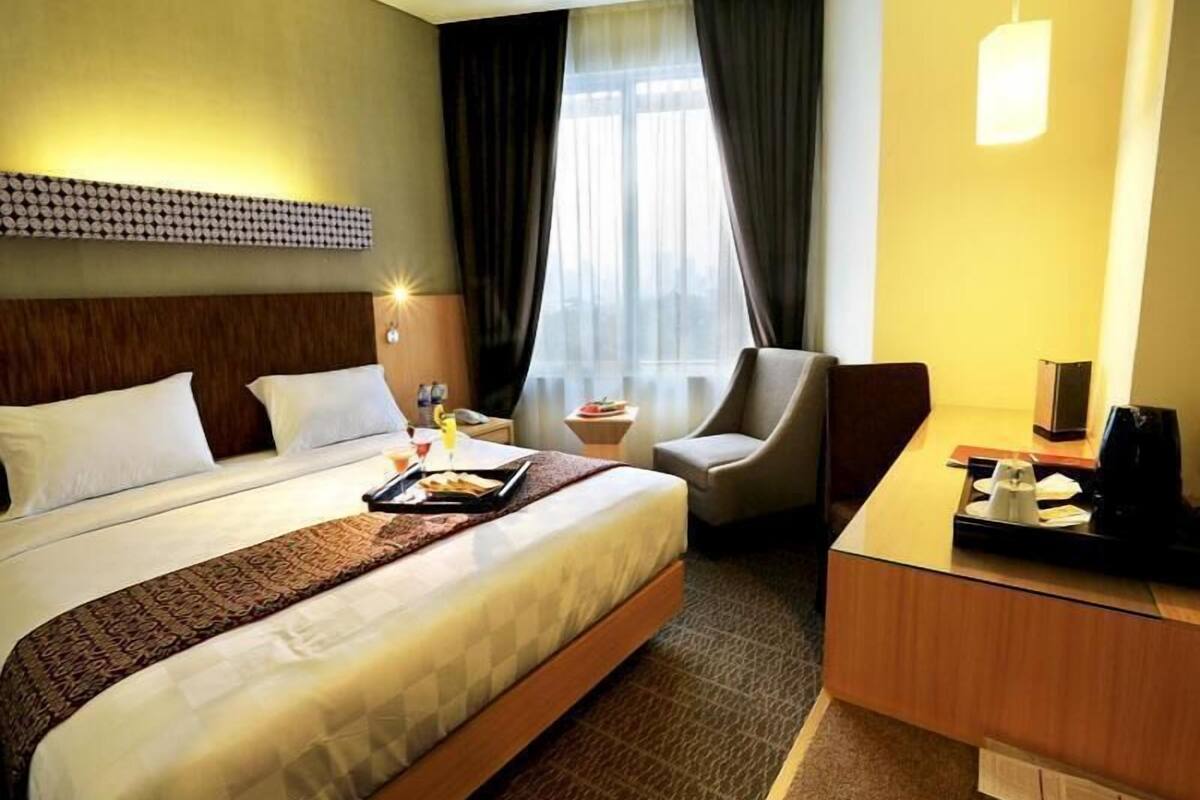 Habitación de hotel con cama, escritorio, silla, mesita de noche y ventana con cortinas.