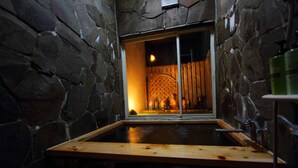 A stone-walled room with a wooden bathtub and a window with a lattice design. - Scotch Court (Nasu)