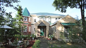 A multi-story house with a stone facade, a green roof, and a front entrance with a green door. - Scotch Court (Nasu)