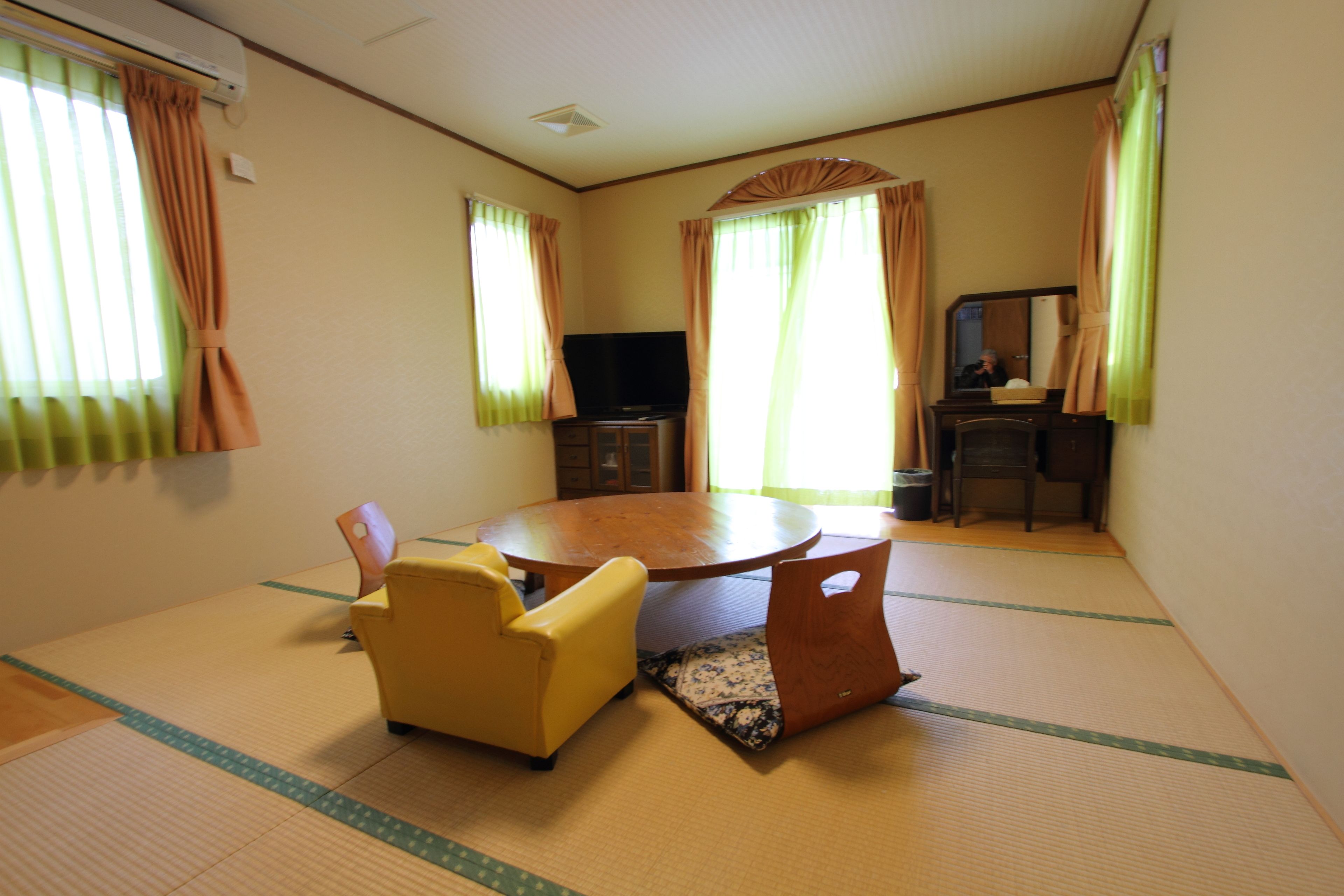 Una habitación con suelo de tatami, una mesa redonda, un sofá y un televisor.