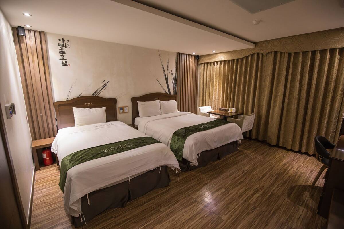 Habitación de hotel con dos camas, una mesita, una silla y suelo de madera.