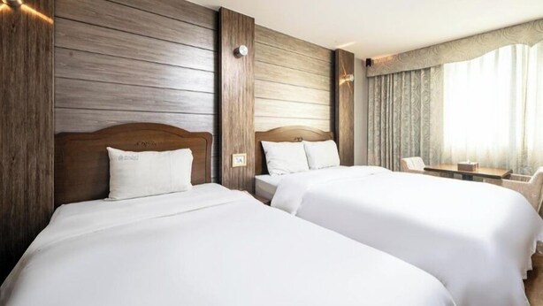 Une chambre d’hôtel avec deux lits, des lambris en bois, un bureau et une grande fenêtre avec des rideaux.