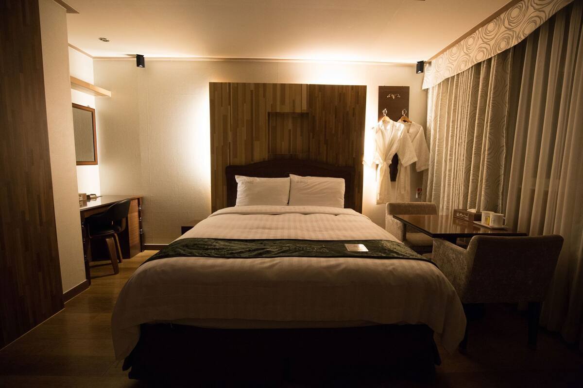 Una habitación de hotel con cama, mesita de noche, silla y escritorio con otra silla.