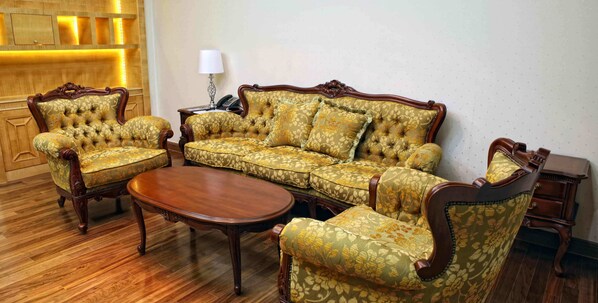 A traditional living room with a sofa set, matching armchairs, a wooden coffee table, and a side table with a lamp.