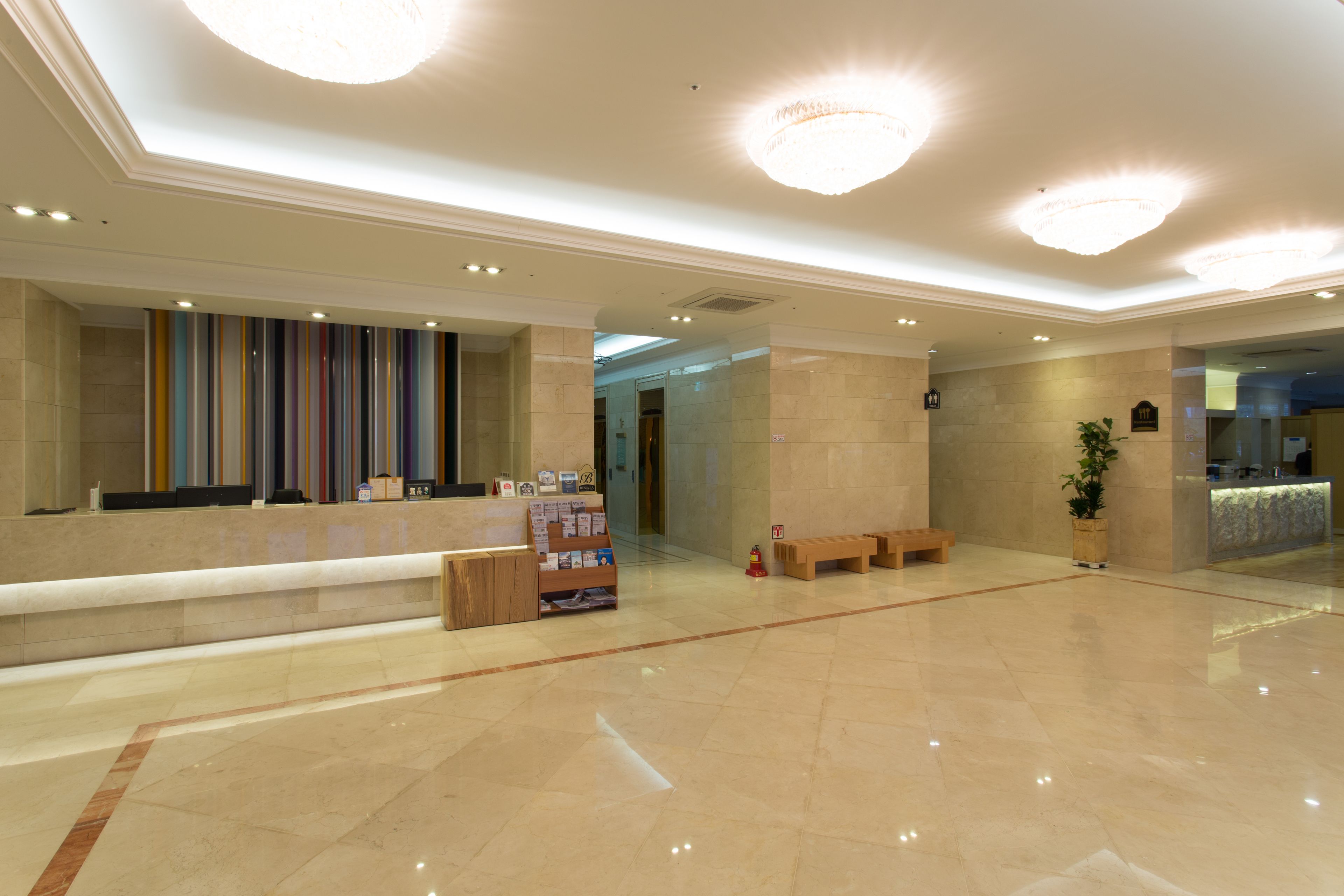A spacious lobby with a reception desk, benches, a plant, and a chandelier.