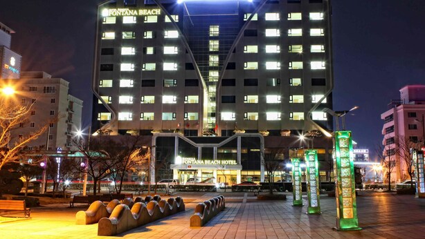 Un hotel de varios pisos con un llamativo letrero que dice 'Hotel Benikea Fontana Beach', que presenta un diseño arquitectónico moderno con un atrio central.