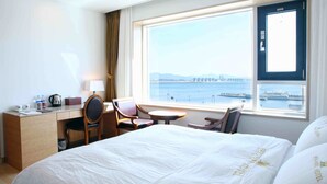 Habitación de hotel con cama, escritorio, silla, mesita y vista a un cuerpo de agua con un puente a lo lejos.