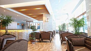 A hotel lobby with a reception desk, seating area, and potted plants.
