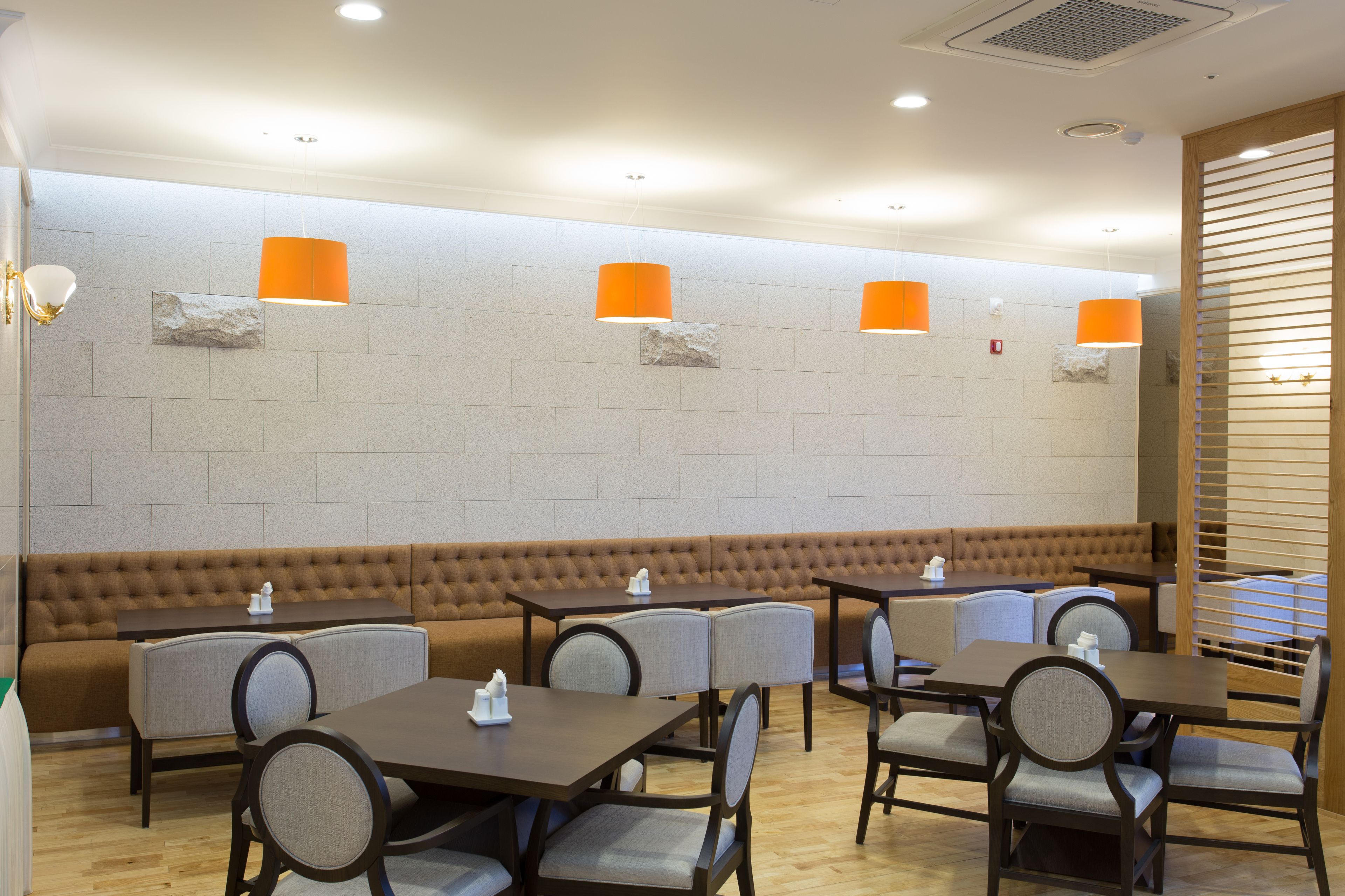 A restaurant with a long brown bench, multiple tables, and orange pendant lights.