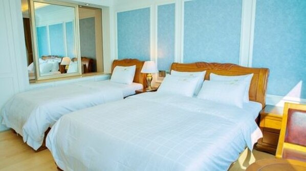 Habitación de hotel con dos camas, un espejo grande y una mesita de noche con lámpara.
