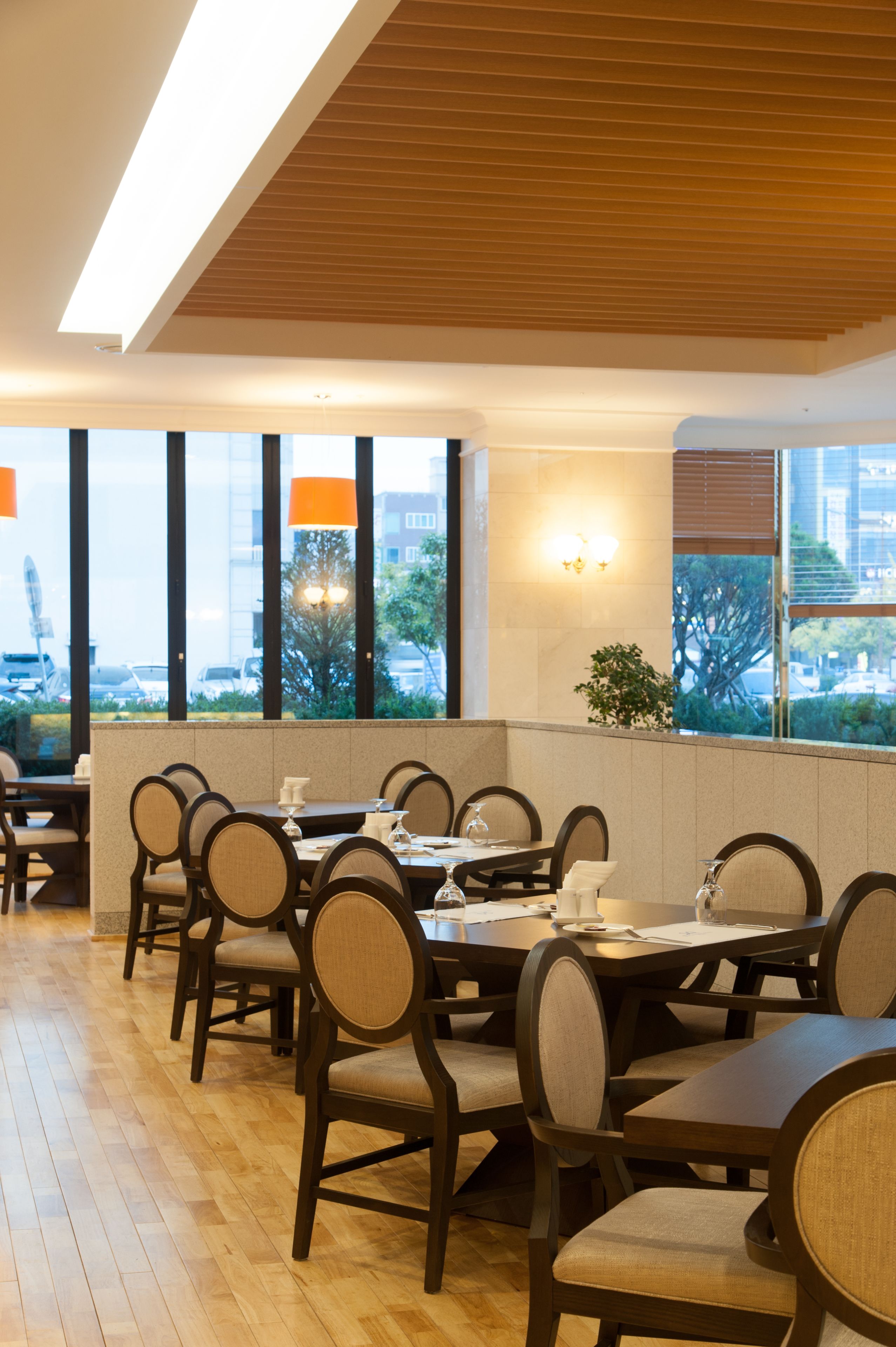 A restaurant with a long table and chairs, large windows, and a view of the city.