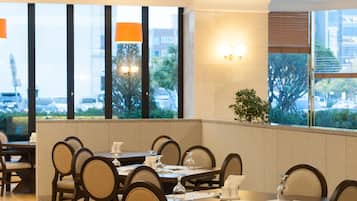 A restaurant with a long table and chairs, large windows, and a view of the city.