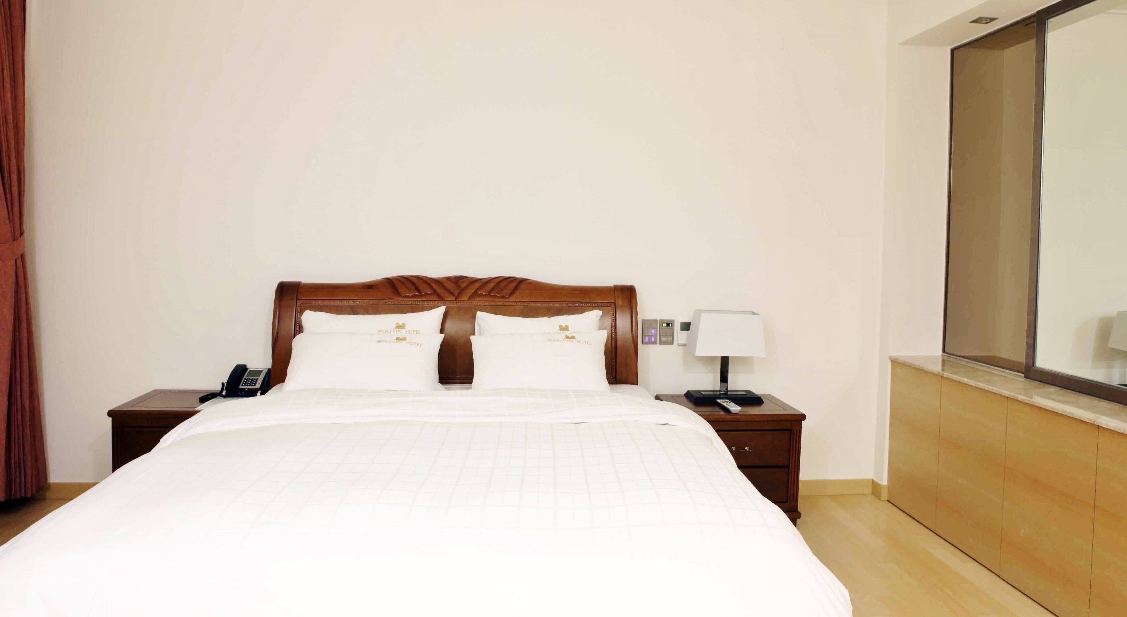 A hotel room with a large bed, two bedside tables, a nightstand with a lamp, a telephone, and a mirror on the wall.