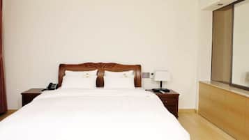 A hotel room with a large bed, two bedside tables, a nightstand with a lamp, a telephone, and a mirror on the wall.