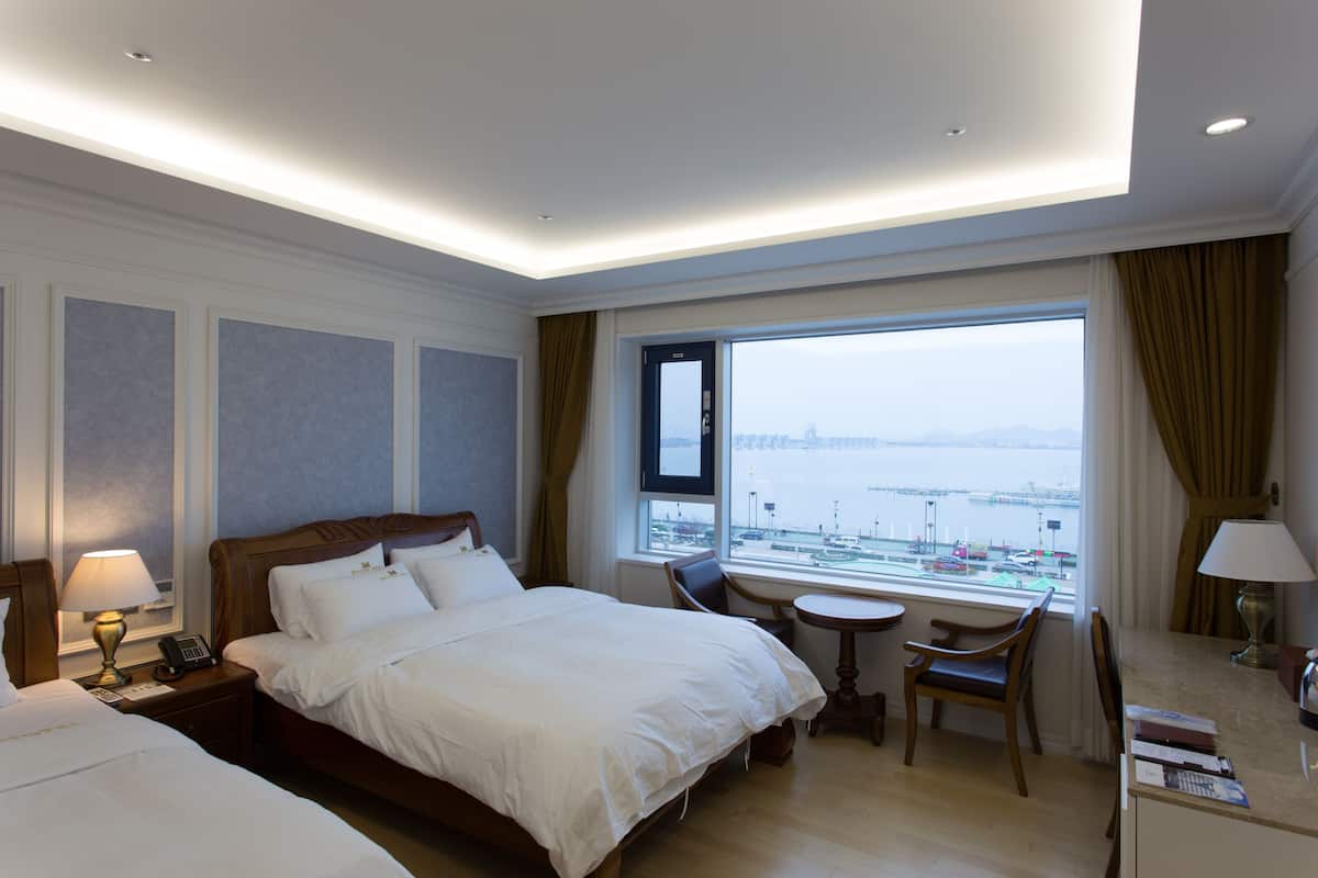 Ein Hotelzimmer mit einem großen Bett, einem Schreibtisch, einem Sessel, einem kleinen Tisch und Blick auf das Wasser.