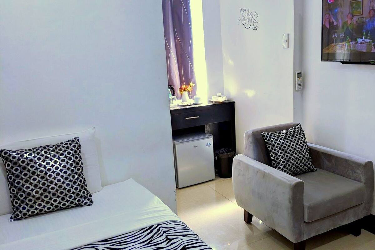 Habitación de hotel con cama, sofá, sillón, una mesita, televisor y kitchenette.
