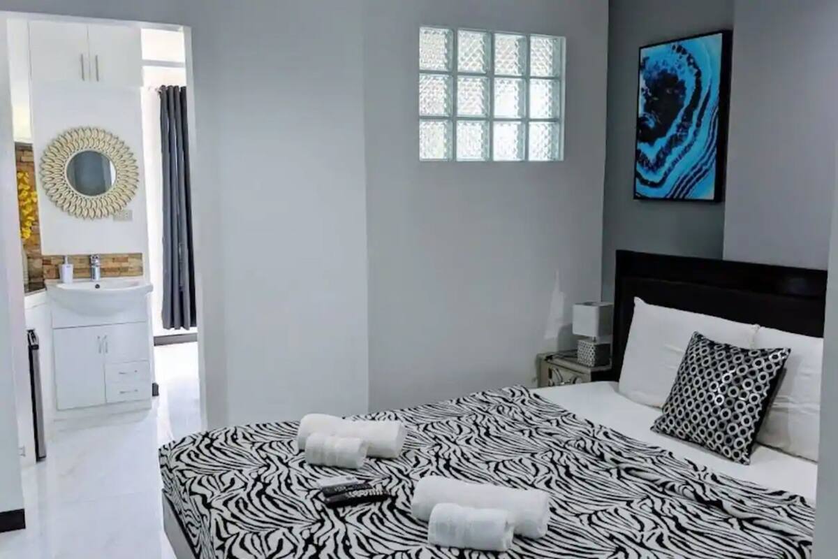 Un dormitorio moderno con una colcha de estampado de cebra, un espejo redondo, una ventana con diseño geométrico y un cuadro abstracto azul.