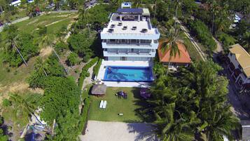 Um hotel moderno com piscina no terraço, cercado por vegetação exuberante e palmeiras.