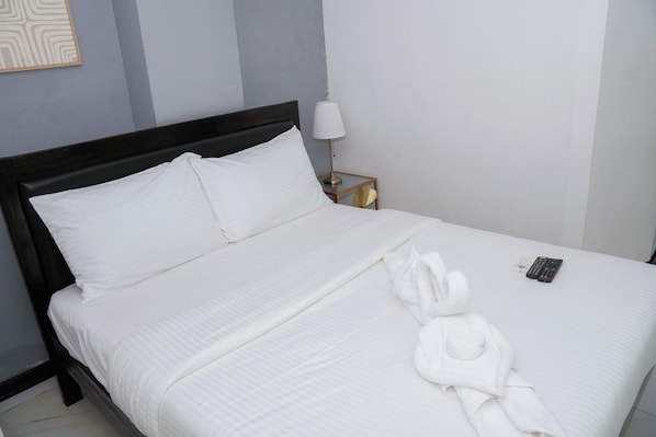 Una cama bien hecha con sábanas blancas, cabecera negra y una toalla blanca con un diseño de corazón sobre la cama.