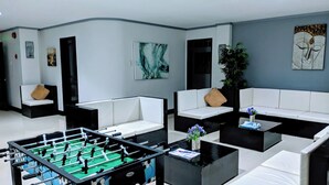 Ein modernes Wohnzimmer mit weißen Sofas, einem Kicker und einem großen Gemälde an der Wand.
