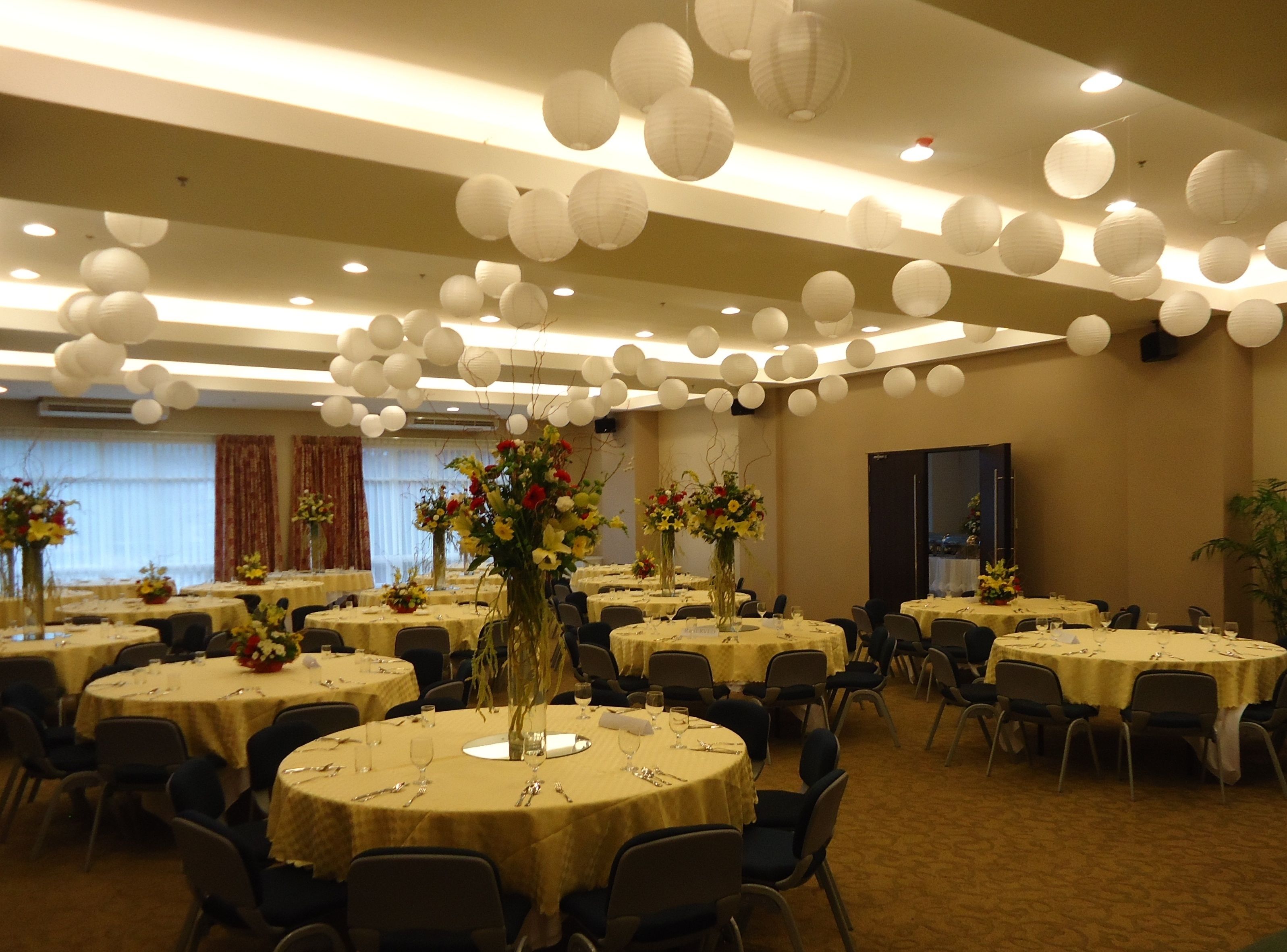 Une salle de banquet avec des tables rondes, des lanternes en papier blanc et des compositions florales en guise de décoration centrale.