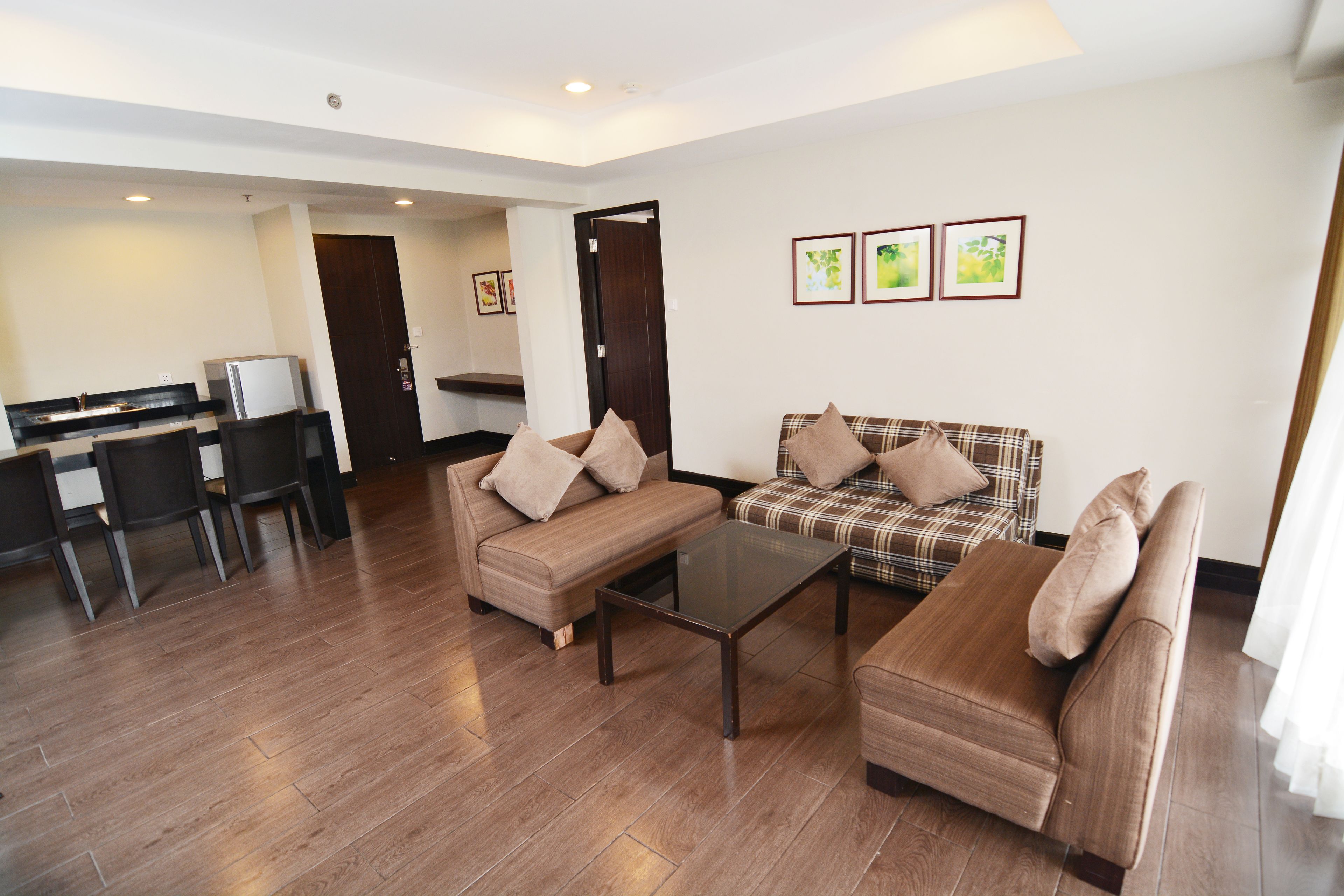 A modern living room with a sofa, a coffee table, and a dining area with chairs and a refrigerator.
