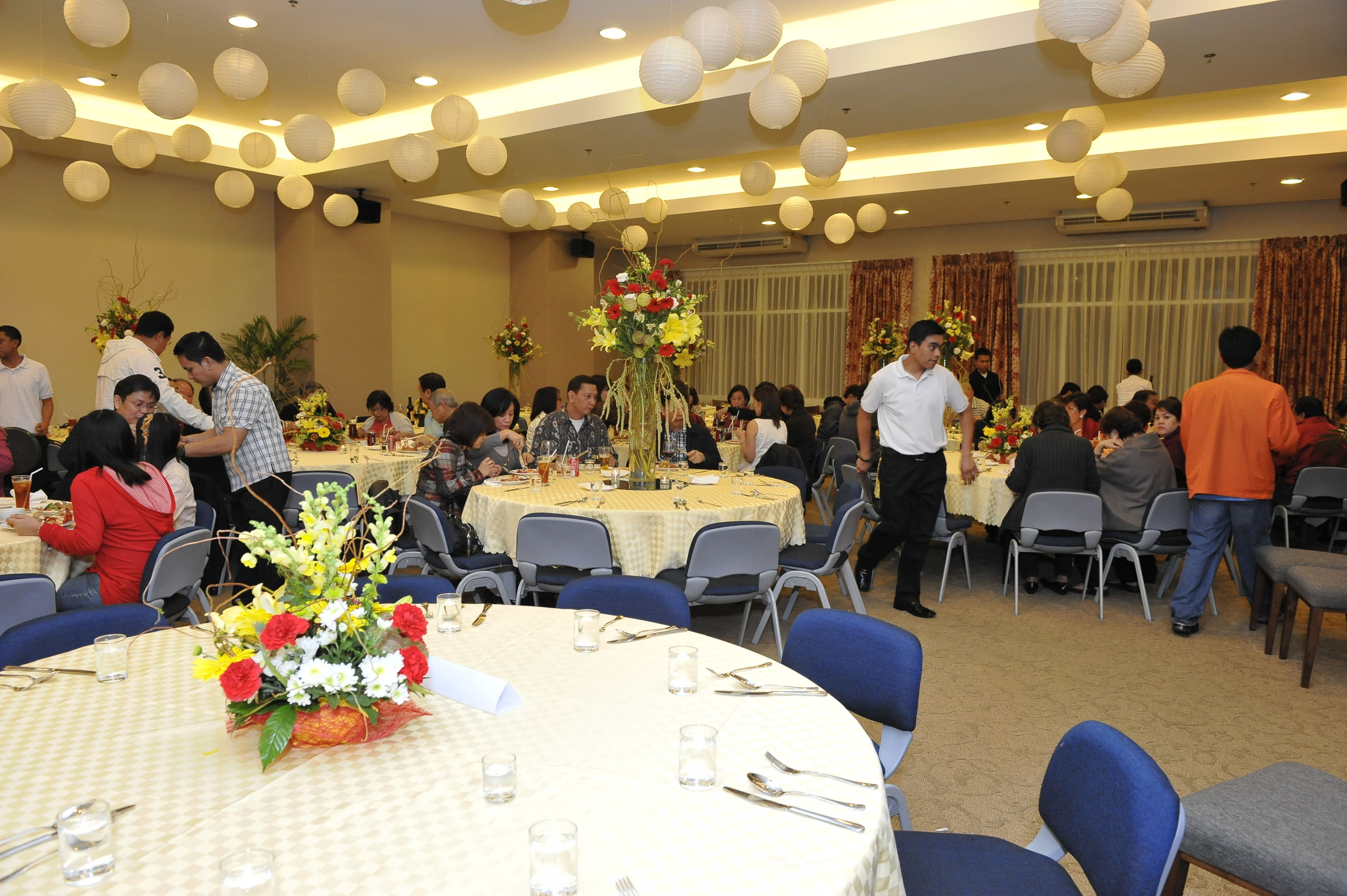 Une salle de banquet avec des tables rondes, des chaises et des centres de table floraux.