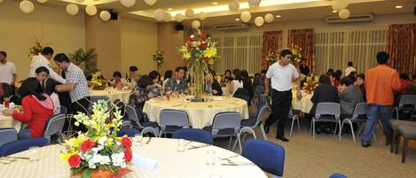 Une salle de banquet avec des tables rondes, des chaises et des centres de table floraux.