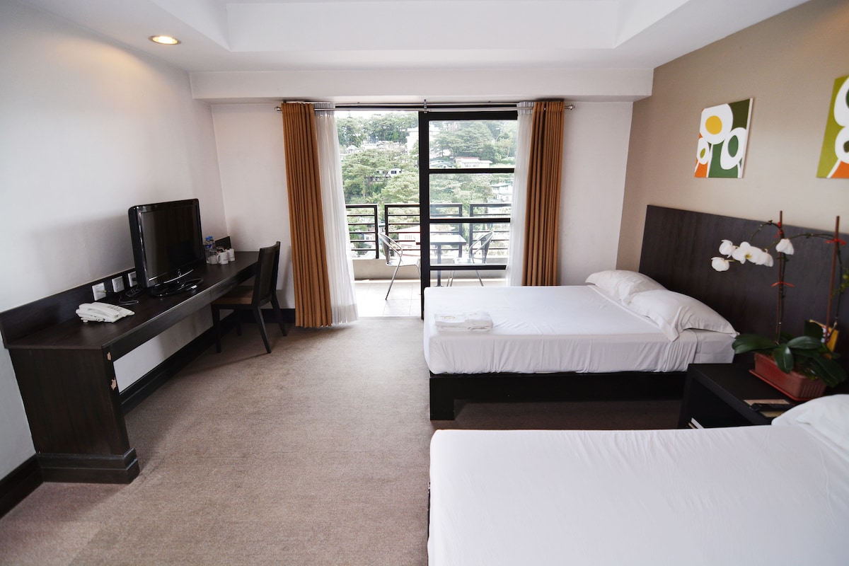 Una habitación de hotel con cama, escritorio con televisor y balcón con vista a la ciudad.