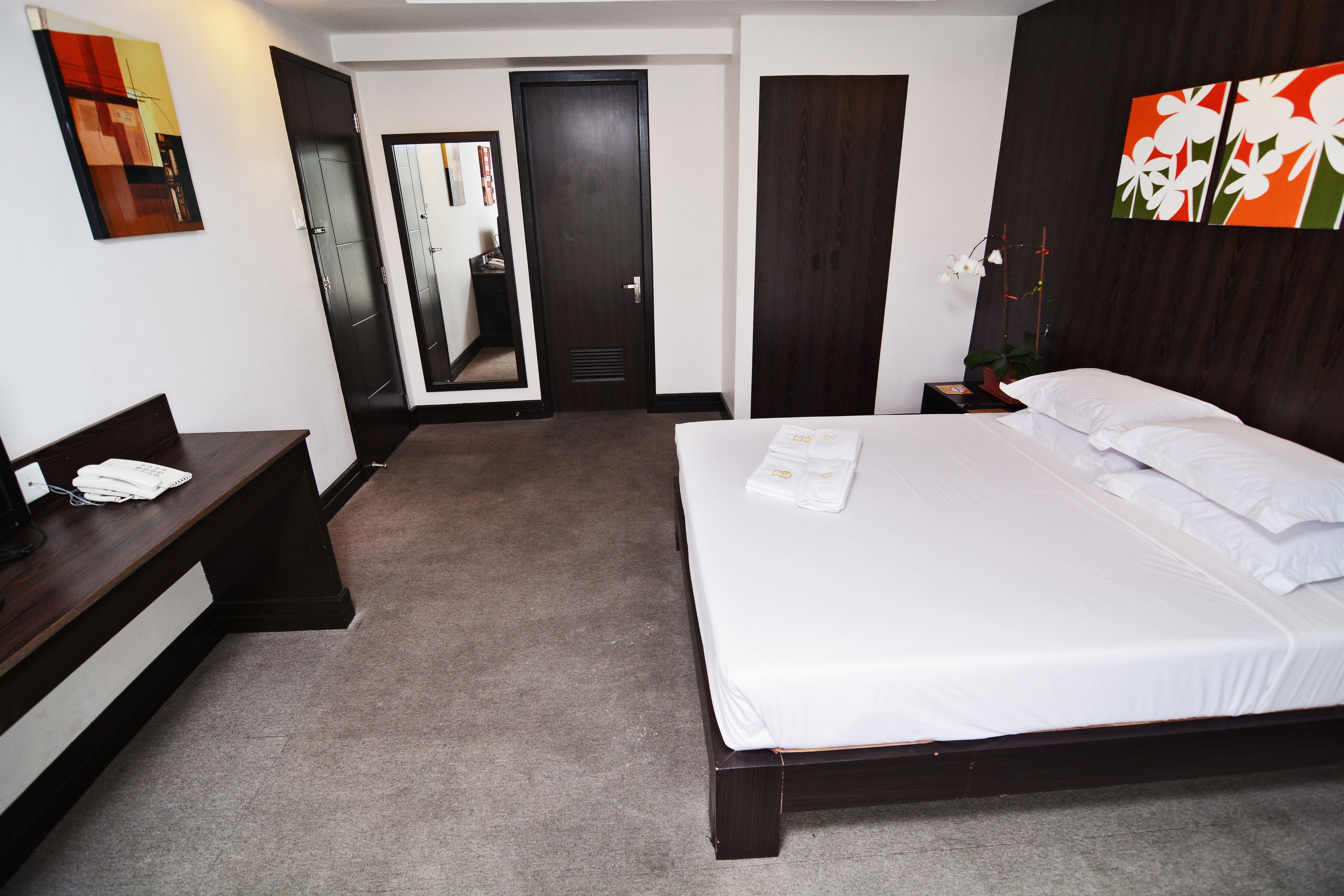 A hotel room with a large bed, a desk, a chair, a wardrobe, and a mirror.