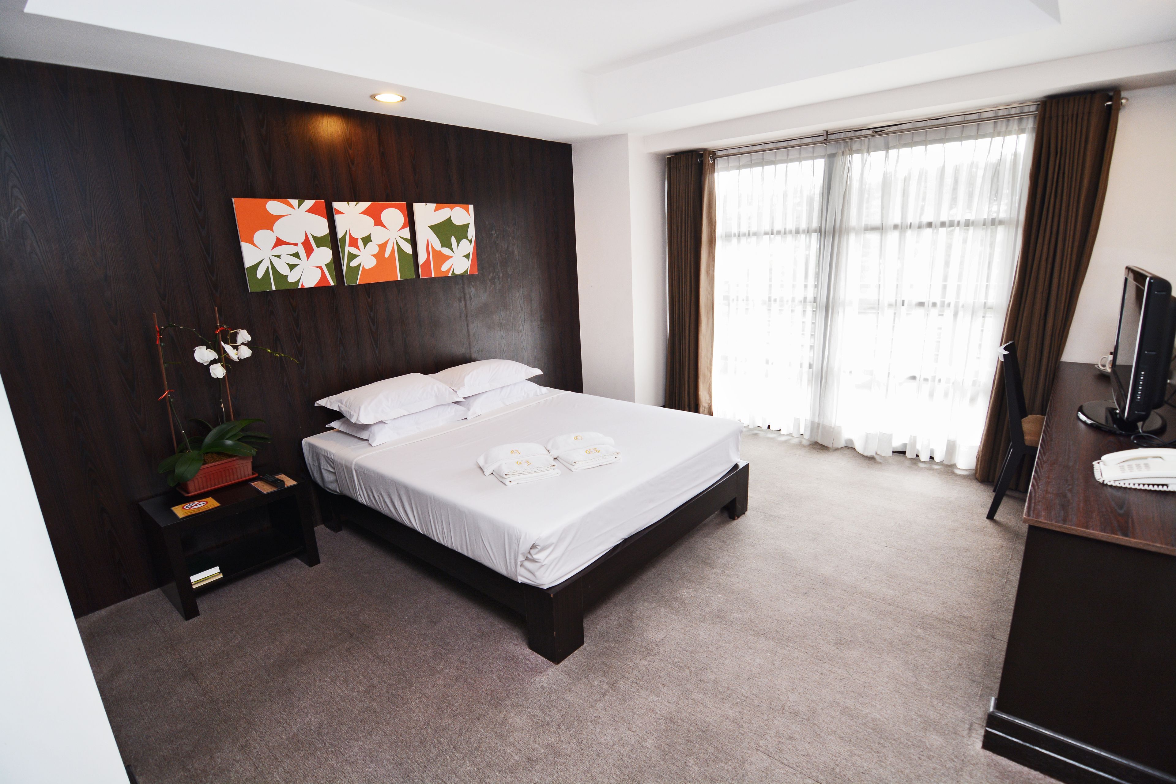 A modern hotel room with a large bed, a nightstand, a desk with a computer, and a window with curtains.