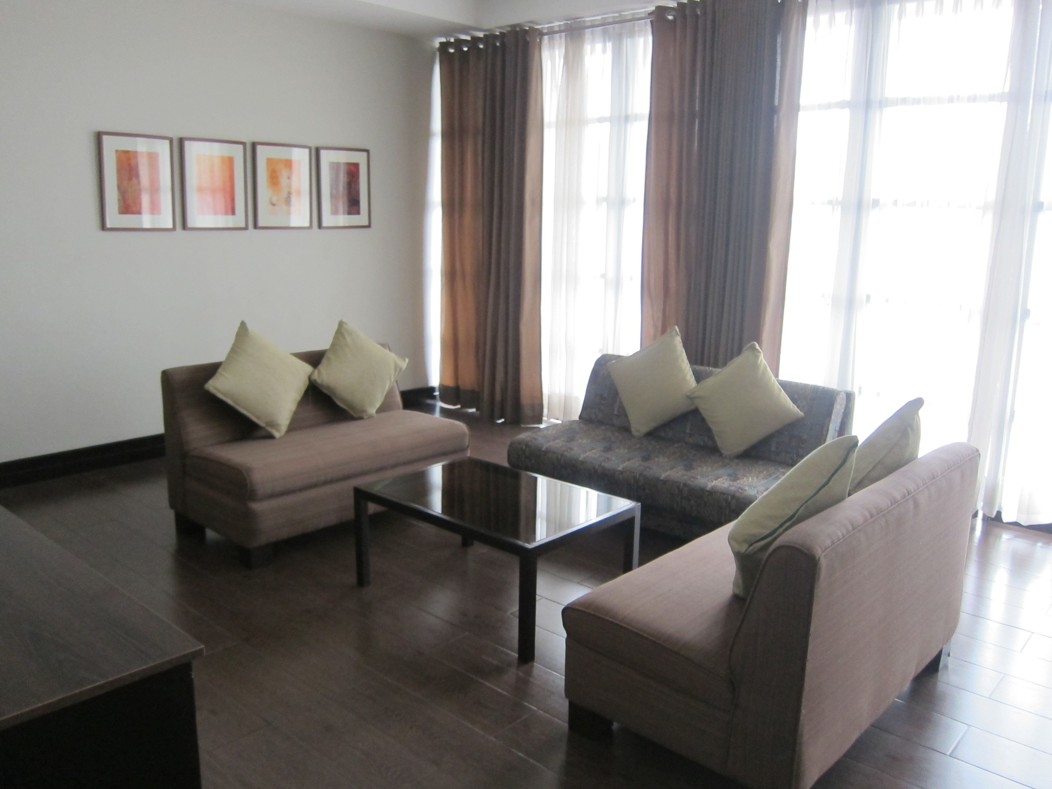 A living room with two sofas, a coffee table, and a TV. There are curtains and framed pictures on the wall.