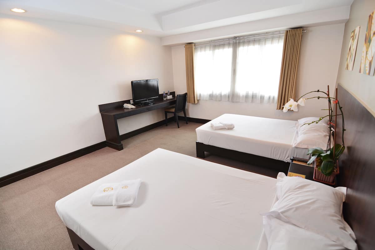 A hotel room with two beds, a desk with a TV, and a window with curtains.