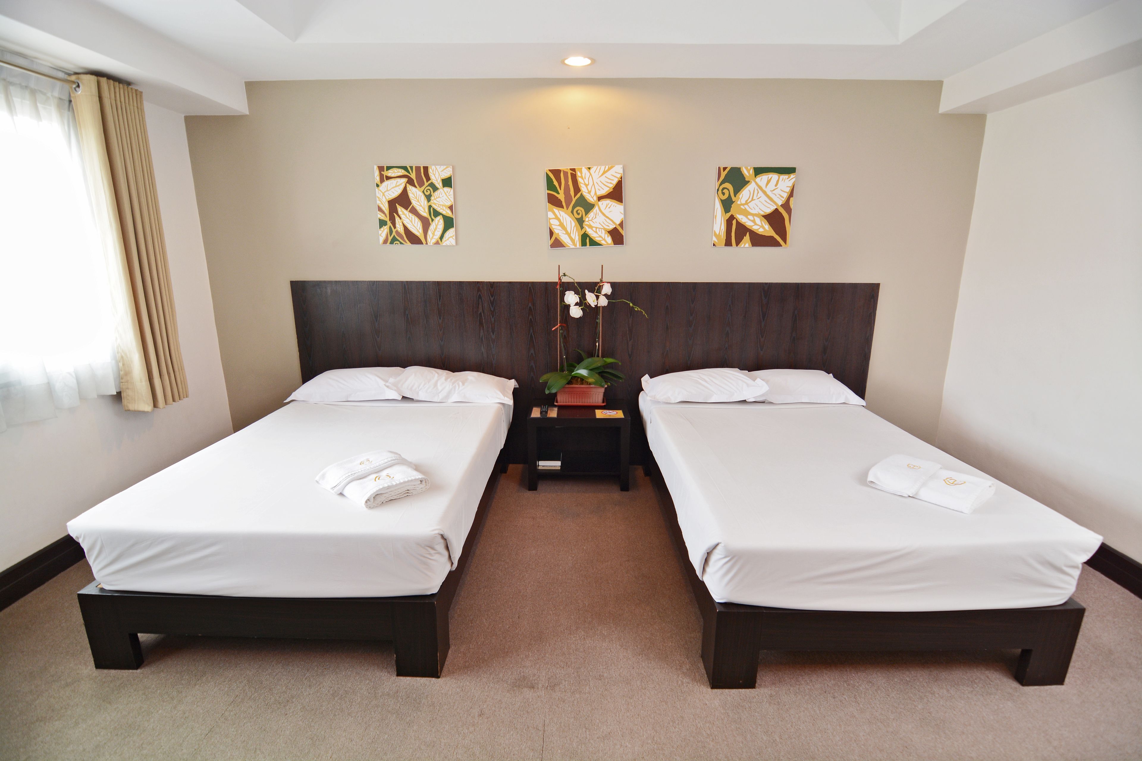 A hotel room with two single beds, a nightstand with a plant, and artwork on the wall.