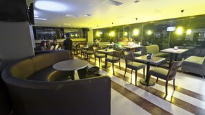 Un hall d’hôtel moderne offrant différents types de sièges, notamment des canapés et des tables, une grande fenêtre donnant sur un paysage agréable et un plafond doté d’un éclairage encastré.