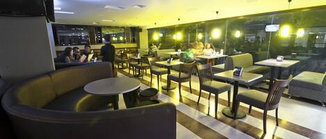 En moderne hotellobby med et udvalg af siddepladser, herunder sofaer og borde, et stort vindue med udsigt og et loft med indbygningsbelysning.