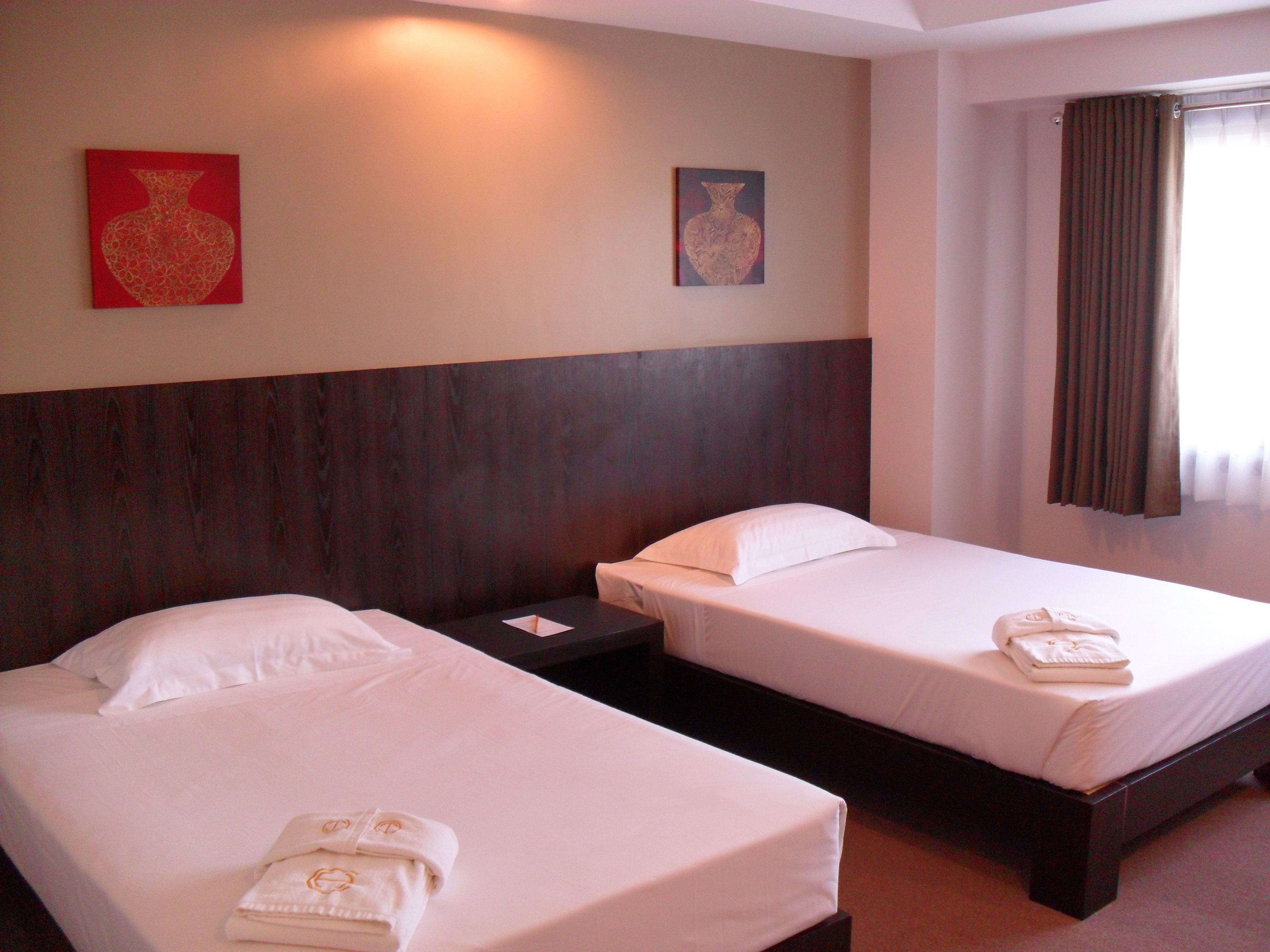 Habitación de hotel con dos camas individuales, una mesita de noche y dos cuadros colgados en la pared.