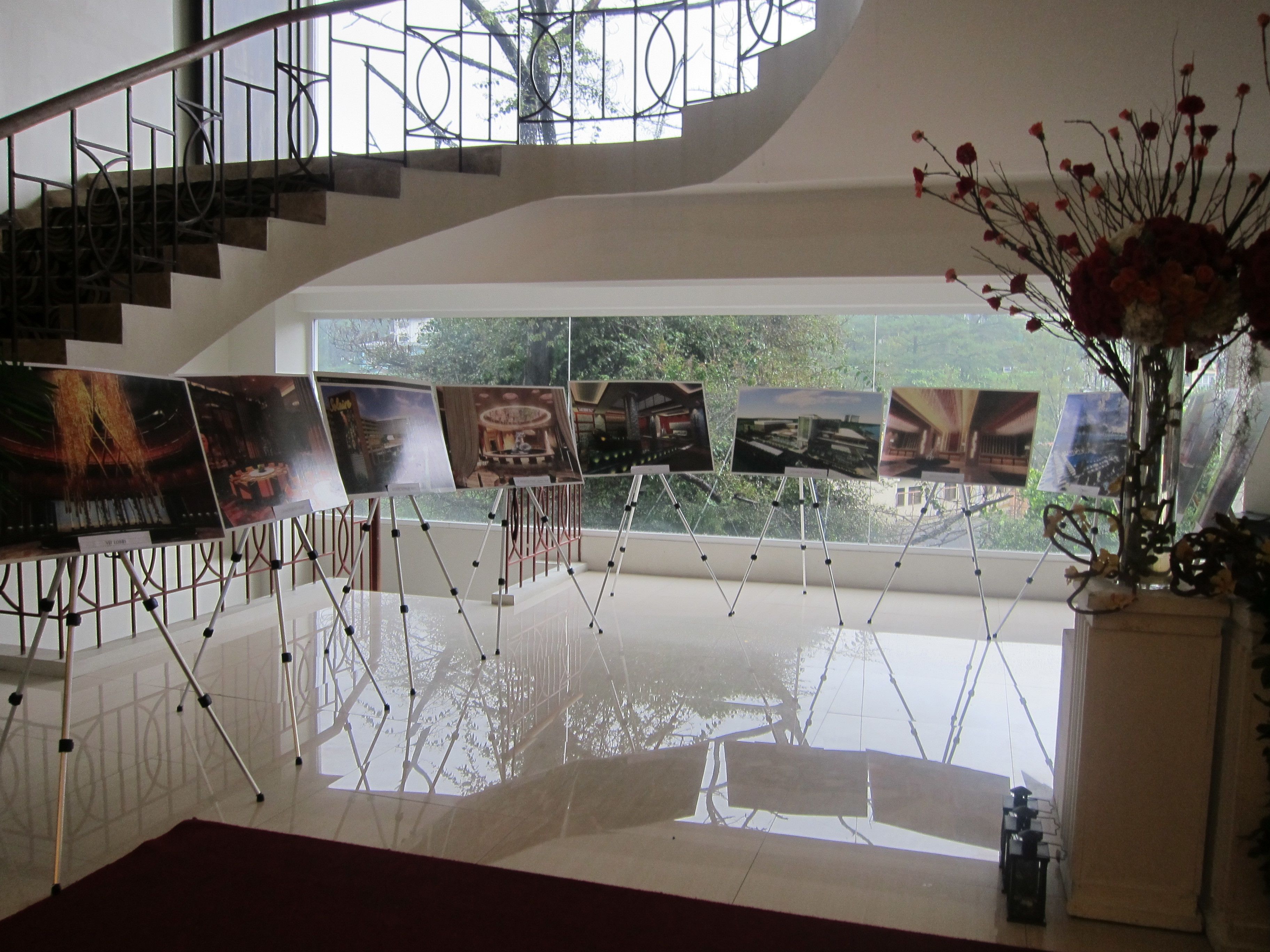 A modern interior with a staircase, a series of framed artworks on easels, and a vase with flowers.