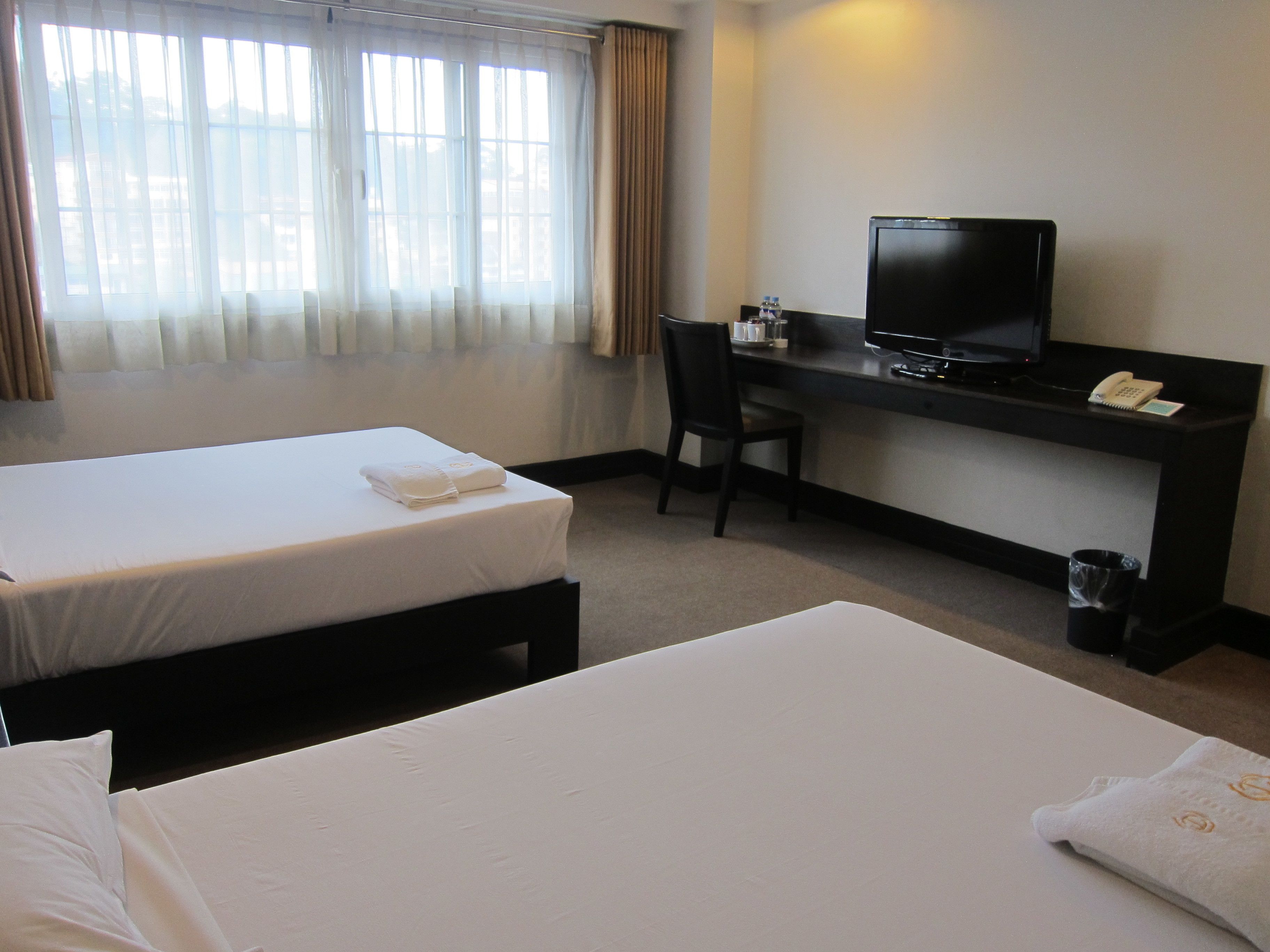 Une chambre d’hôtel avec deux lits, un bureau avec une télévision et une chaise.