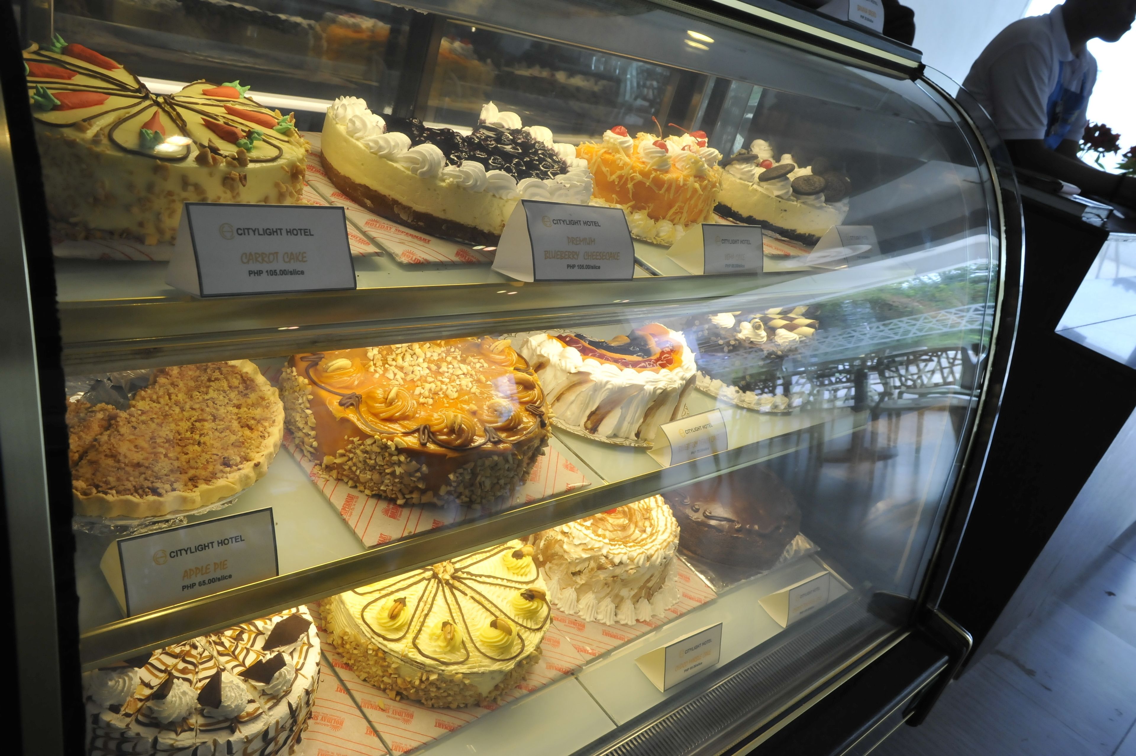 A display case with various cakes, including carrot cake, blueberry cheesecake, and apple pie.