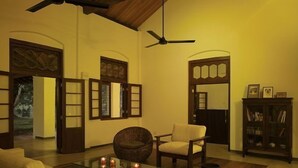 Una sala de estar con sofá, sillones, una mesa de centro de vidrio con velas, ventilador de techo y estantería.